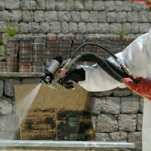 a man in a white coverall spraying water on a brick wall